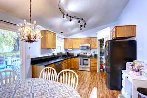Kitchen with dark countertops, appliances with stainless steel finishes, a textured ceiling, vaulted ceiling, and brown cabinetry