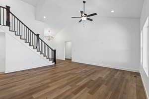 Unfurnished living room with dark wood-type flooring, high vaulted ceiling, stairs, ceiling fan, and a chandelier