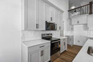 Kitchen with stainless steel appliances, tasteful backsplash, dark wood-type flooring, light stone counters, and white cabinets
