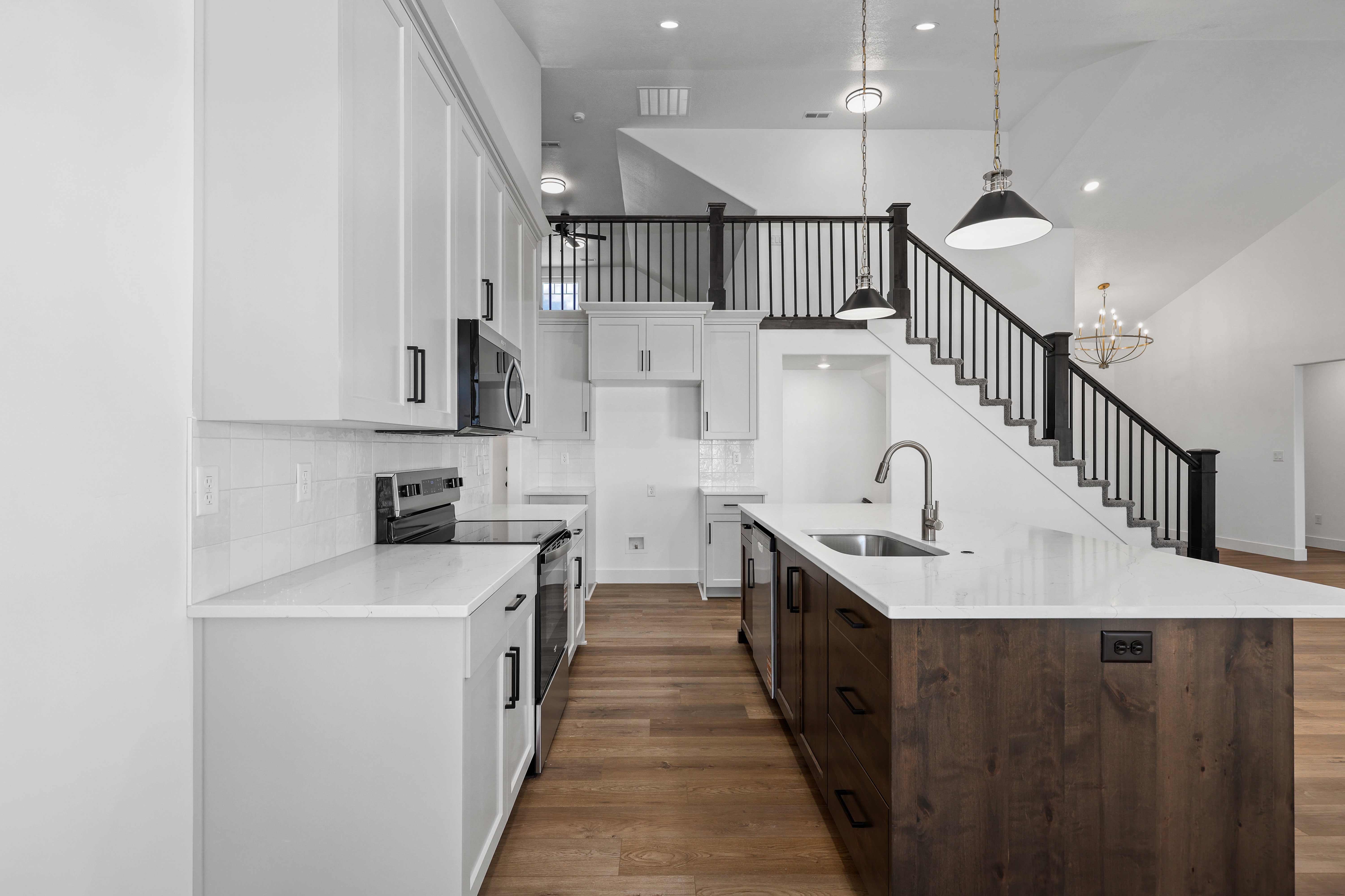 Kitchen with high vaulted ceiling, white cabinets, appliances with stainless steel finishes, dark wood-style floors, and a center island with sink
