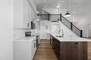 Kitchen with high vaulted ceiling, white cabinets, appliances with stainless steel finishes, dark wood-style floors, and a center island with sink