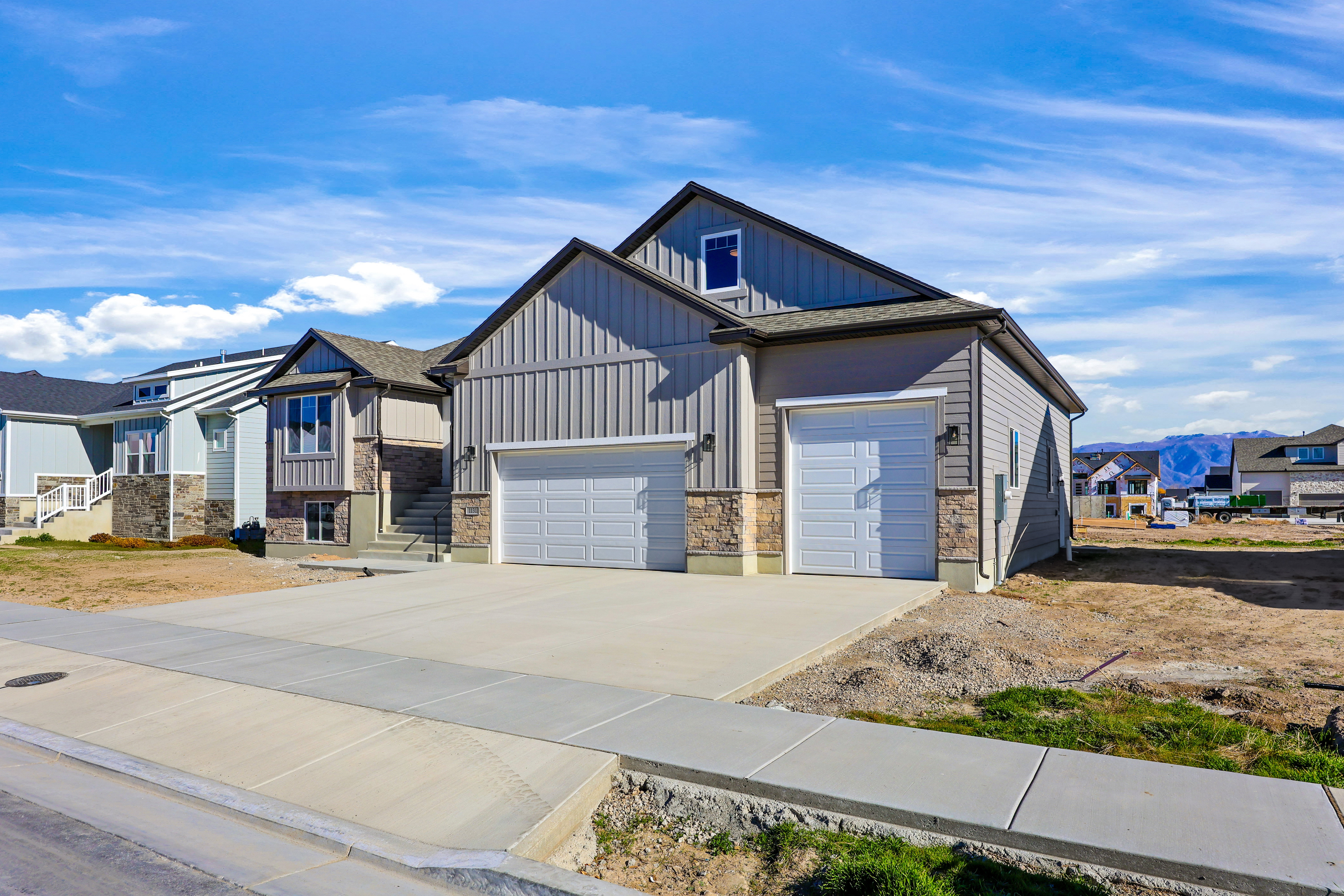 View of front of home featuring board and batten siding, concrete driveway, stone siding, a residential view, and a mountain view