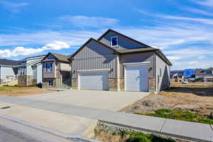 View of front of home featuring board and batten siding, concrete driveway, stone siding, a residential view, and a mountain view