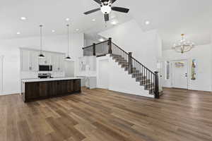 Kitchen featuring high vaulted ceiling, open floor plan, pendant lighting, dark brown cabinets, and a kitchen island with sink