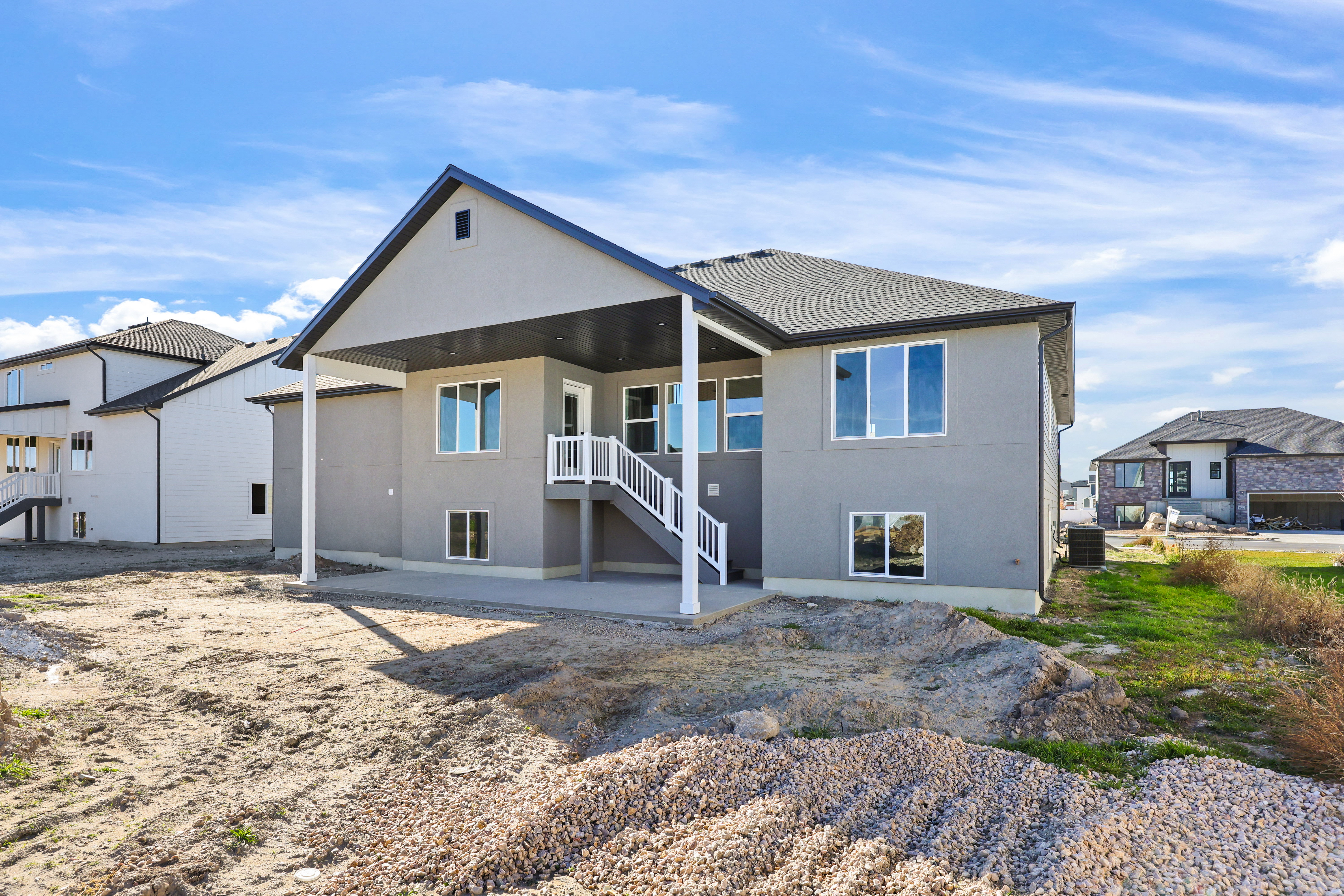 Rear view of house featuring a patio, stucco siding, a shingled roof, and stairs