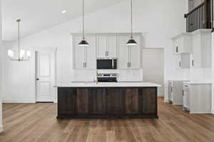 Kitchen featuring white cabinetry, an island with sink, high vaulted ceiling, backsplash, and pendant lighting