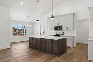 Kitchen with a kitchen island with sink, stainless steel appliances, hanging light fixtures, dark brown cabinetry, and tasteful backsplash