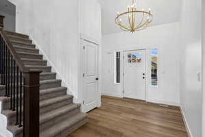 Entryway featuring wood finished floors, stairway, a chandelier, and a towering ceiling