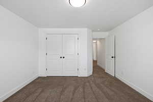 Unfurnished bedroom featuring dark carpet, a closet, and a textured ceiling