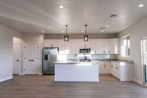 Kitchen featuring hanging light fixtures, appliances with stainless steel finishes, an island with sink, white cabinetry, and recessed lighting