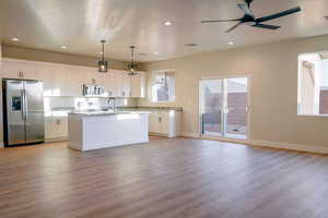 Kitchen featuring stainless steel appliances, pendant lighting, white cabinetry, an island with sink, and light wood-style flooring