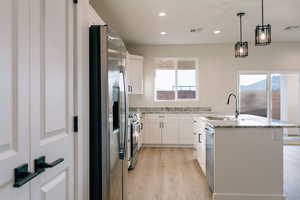 Kitchen featuring stainless steel appliances, a kitchen island with sink, hanging light fixtures, white cabinets, and recessed lighting