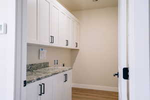 Washroom featuring cabinet space, light wood finished floors, washer hookup, and hookup for an electric dryer