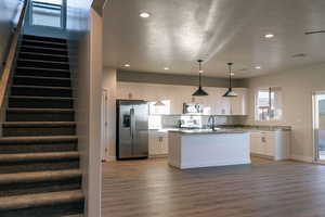 Kitchen with stainless steel appliances, white cabinets, hanging light fixtures, a kitchen island with sink, and dark wood-style flooring