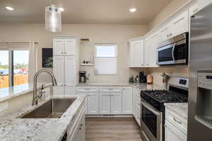 Kitchen featuring appliances with stainless steel finishes, white cabinets, decorative light fixtures, light wood-style floors, and recessed lighting