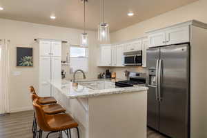 Kitchen with appliances with stainless steel finishes, dark wood-style flooring, hanging light fixtures, light stone countertops, and white cabinets