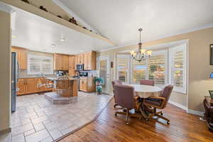 Dining space with light wood-style floors, vaulted ceiling, ornamental molding, a textured ceiling, and a chandelier