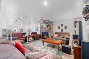 Living room featuring a textured ceiling, wood finished floors, a fireplace, a ceiling fan, and recessed lighting