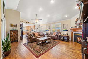 Living room with crown molding, a ceiling fan, light wood finished floors, a tiled fireplace, and lofted ceiling