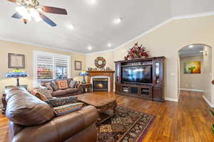 Living room with arched walkways, lofted ceiling, wood finished floors, crown molding, and a glass covered fireplace