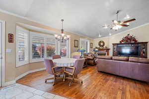 Dining room with a fireplace, a chandelier, crown molding, light wood-style flooring, and a ceiling fan