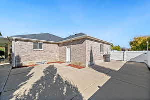 View of property exterior with a gate, brick siding, roof with shingles, and a patio