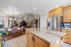Kitchen featuring light stone countertops, ceiling fan, crown molding, stainless steel refrigerator with ice dispenser, and a chandelier