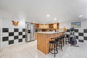 Kitchen featuring a peninsula, a kitchen breakfast bar, stainless steel fridge, light tile patterned floors, and recessed lighting