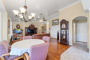 Dining area featuring ornamental molding, arched walkways, light wood-type flooring, vaulted ceiling, and ceiling fan