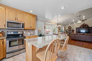 Kitchen featuring appliances with stainless steel finishes, light stone countertops, a breakfast bar area, a chandelier, and a lit fireplace