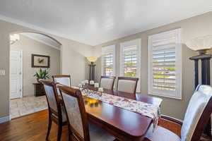 Dining area with healthy amount of natural light, crown molding, dark wood-type flooring, arched walkways, and a textured ceiling