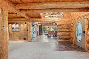 Foyer entrance featuring carpet flooring, a chandelier, a wooden ceiling with exposed beams, log walls, and tile patterned floors