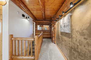 Hallway featuring log walls, light carpet, a wood ceiling with exposed beams, a barn door, and an upstairs landing
