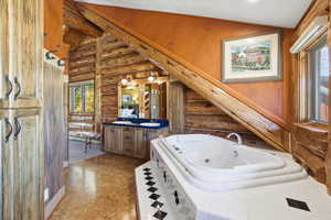 Full bathroom featuring a tub with jets, log walls, double vanity, and vaulted ceiling