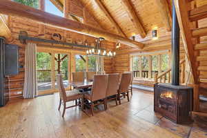 Dining space with high vaulted ceiling, light wood-type flooring, a wood stove, log walls, and a wooden ceiling with exposed beams