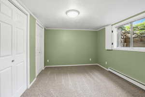 Unfurnished bedroom featuring baseboard heating, light colored carpet, a textured ceiling, and multiple closets