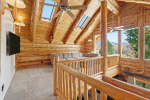 Unfurnished bedroom with rustic walls, wooden ceiling, a skylight, a mountain view, and light colored carpet