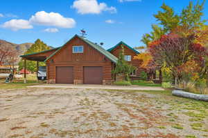 Log cabin featuring log exterior, a carport, a garage, and stone siding
