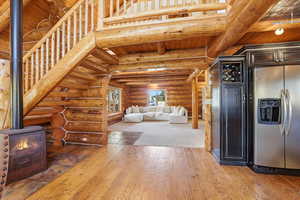 Unfurnished living room with log walls, a wood ceiling with exposed beams, a wood stove, and light wood-style floors