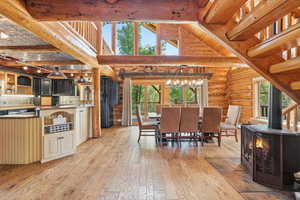 Dining area with a wood stove, plenty of natural light, light wood-style flooring, a towering ceiling, and rustic walls