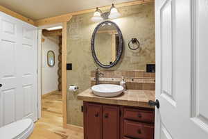 Bathroom featuring wallpapered walls, vanity, tasteful backsplash, and light wood-style flooring