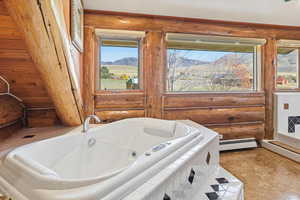 Full bathroom featuring a jetted tub, a baseboard heating unit, rustic walls, and a mountain view