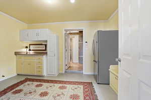 Kitchen featuring freestanding refrigerator, crown molding, white cabinets, and finished concrete flooring