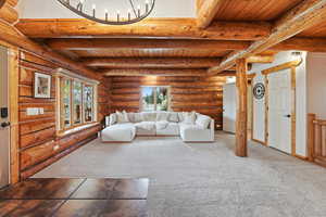 Carpeted living area with log walls, a wooden ceiling with exposed beams, and a chandelier