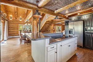 Kitchen with dark stone countertops, hanging light fixtures, dark wood-style floors, appliances with stainless steel finishes, and rustic walls