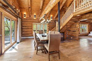 Dining room with high vaulted ceiling, light wood-type flooring, a chandelier, log walls, and stairway