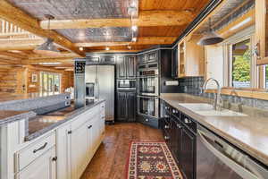 Kitchen featuring pendant lighting, dark cabinetry, beam ceiling, dark wood finished floors, and appliances with stainless steel finishes