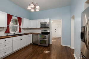 Kitchen featuring stainless steel appliances, white cabinetry, pendant lighting, dark wood-style floors, and tasteful backsplash