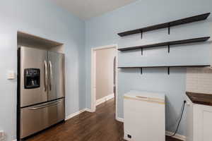 Kitchen featuring stainless steel fridge with ice dispenser, butcher block counters, dark wood-type flooring, backsplash, and white cabinetry