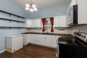 Kitchen with stainless steel appliances, white cabinets, open shelves, dark wood-style flooring, and tasteful backsplash